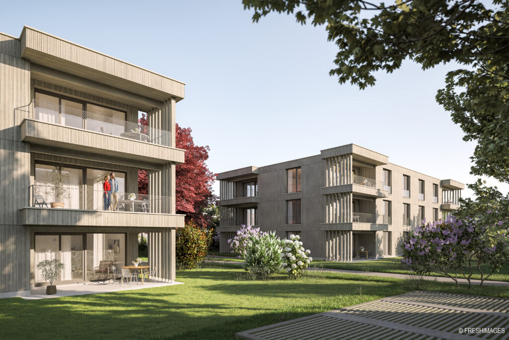Moderne Wohnblocks mit großzügigen Balkonen blicken auf eine gepflegte Rasenfläche und blühende Sträucher; auf einem der Balkone stehen Menschen unter strahlend blauem Himmel, umgeben von Bäumen.