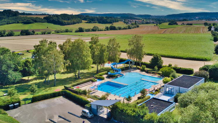 Freibad mit Rutsche mit Bäumen und Wiesen drumherum